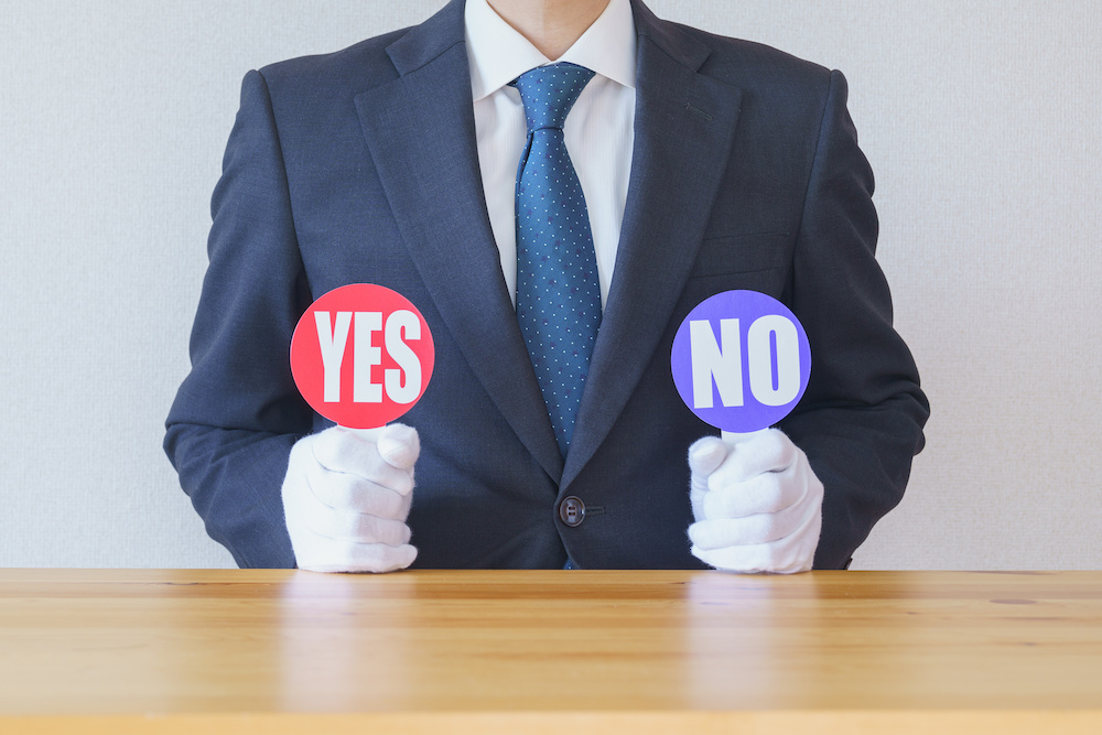 スーツ姿の人がYESとNOのフリップを持っている